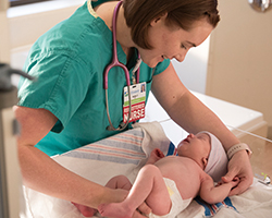 A nurse smiles at a newborn baby in the birthing center.