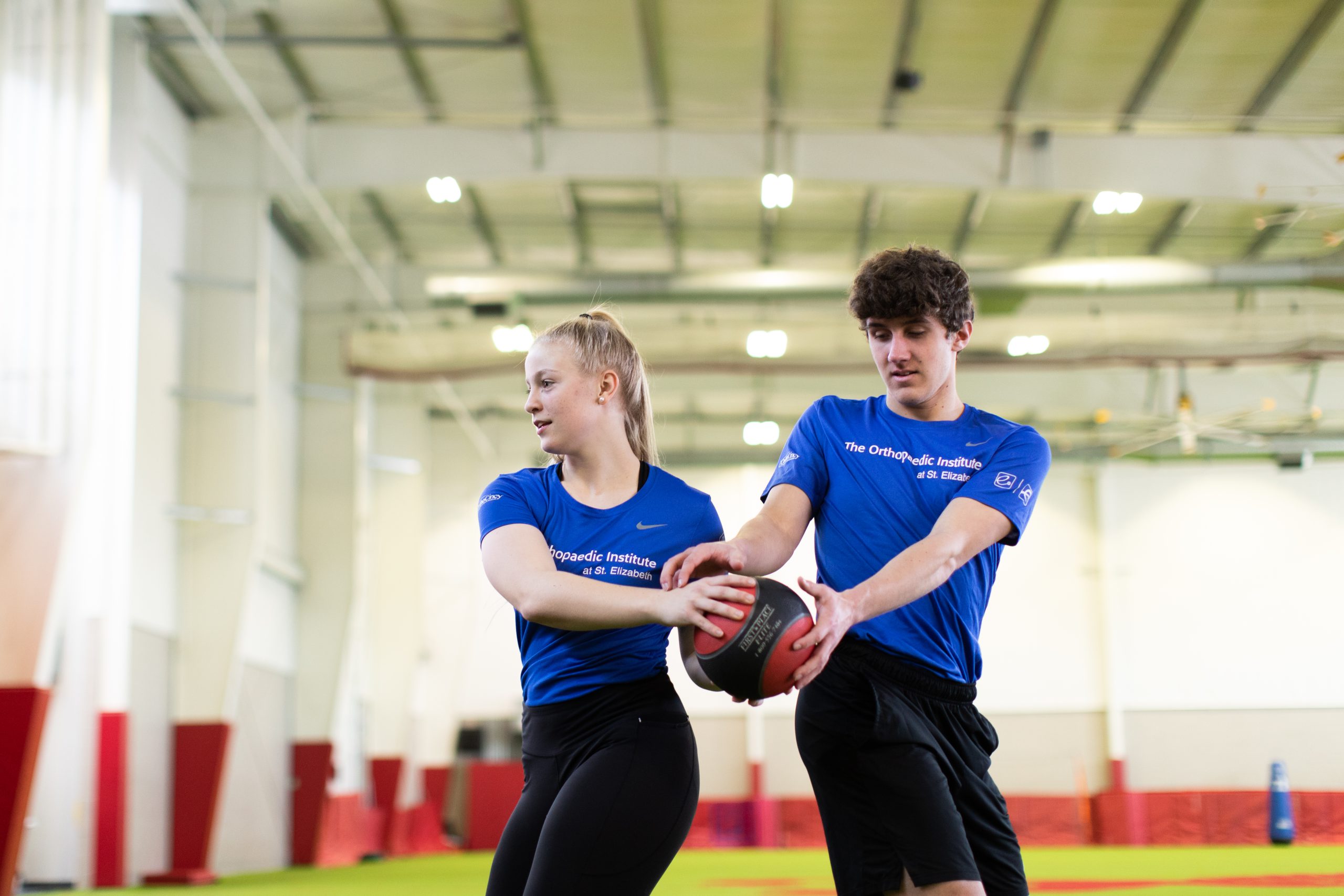 Two Student Athletes exercise with a weighted medicine ball. 