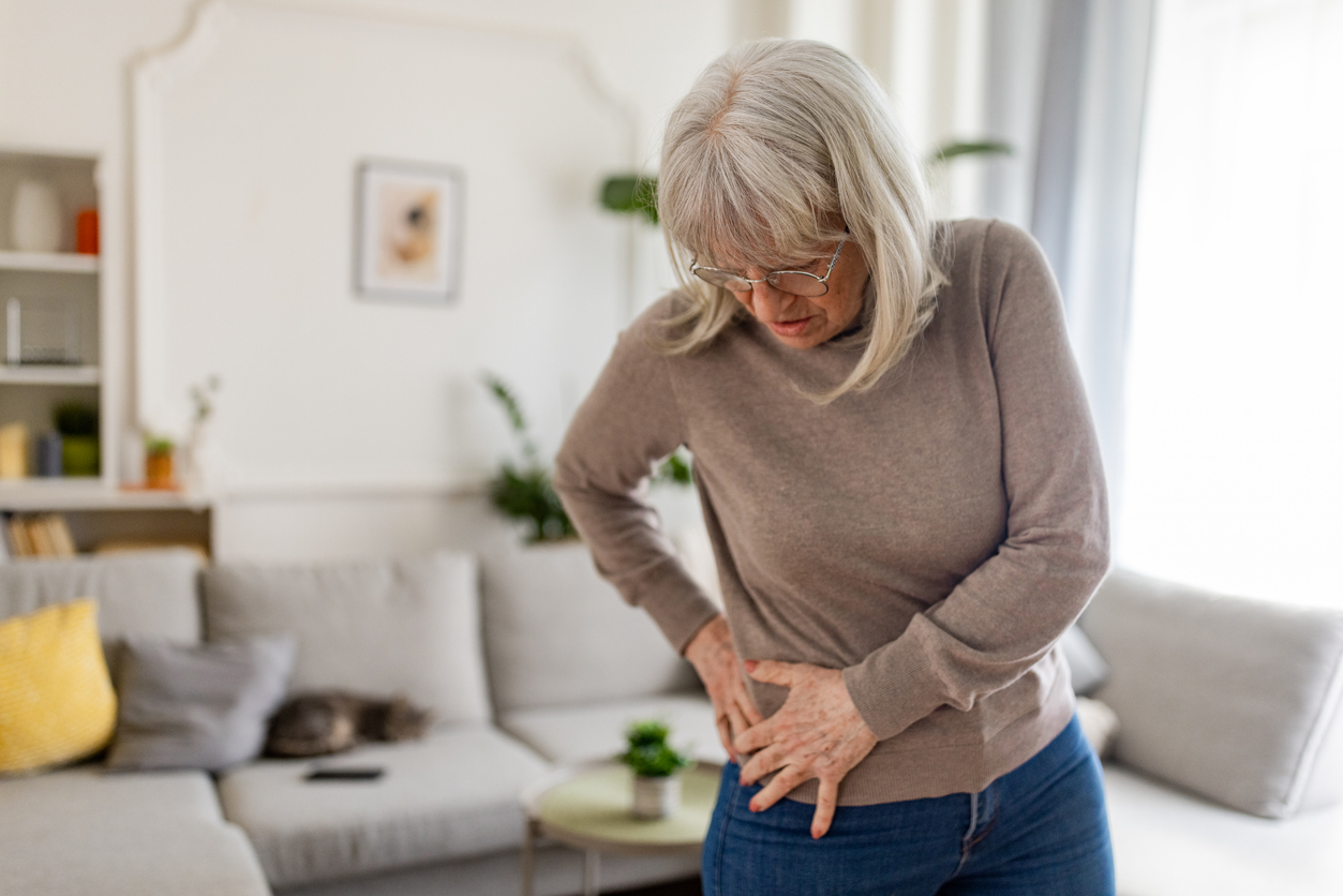 Senior woman having problems with hip pain while standing in living room at home.